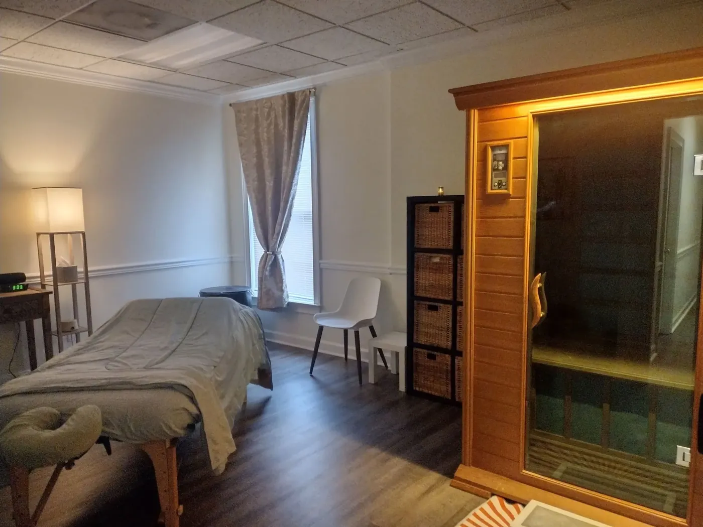 The treatment room at low light, with the massage table, lamp glow, and the infrared sauna